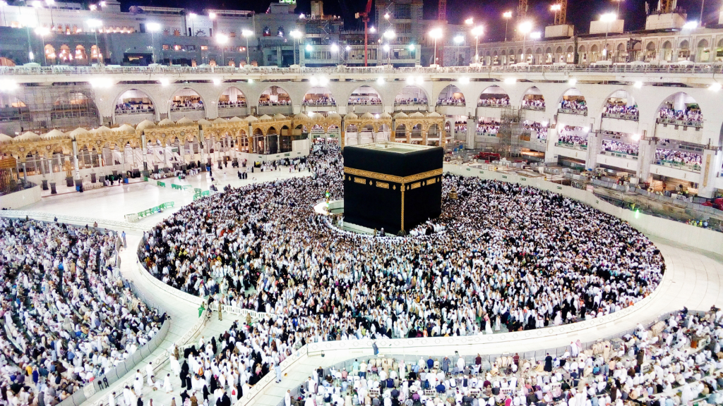 Thousands of pilgrims gather around the Kaaba in the Grand Mosque of Mecca, performing Tawaf as part of the Hajj pilgrimage, with the mosque’s multi-story colonnades filled with additional worshippers.