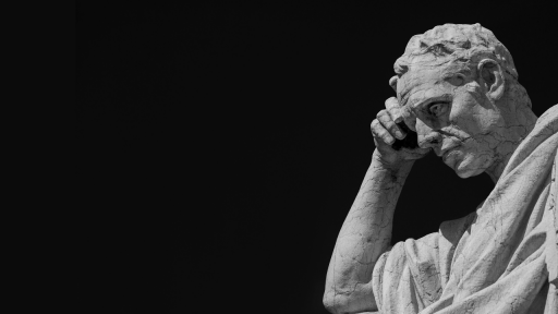 A grayscale image of a weathered stone statue of a man resting his head on his hand, appearing deep in thought, set against a dark, empty background.